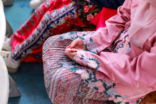 sitting with hands gently folded over an Indonesian batik patterned fabric.