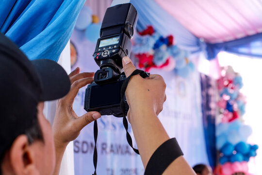 A photographer holding a professional black DSLR camera equipped with a large external flash unit high up to take a picture