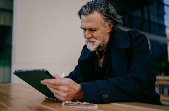 Concentrated middle aged man writing on digital tablet with stylus, profile of mature professional signing electronic document or taking notes at wooden table, remote work, fintech, online banking.