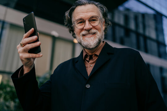 Happy senior executive with cellphone, cheerful male leader using high speed 5G internet for business communication in urban city environment, career growth, financial freedom, social media influencer
