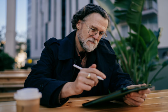 Mature pensive businessman thinking with coffee to go, senior professional looking away thoughtfully near digital tablet at outdoor workspace, career growth, financial freedom, ambition.