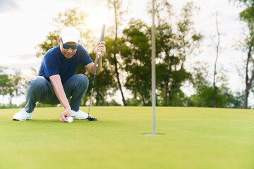 Obraz premium Male golfer placing and aiming golf ball on putting green