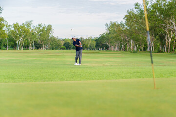 Obraz premium Distant view of an asian golfer hitting a ball towards the green.
