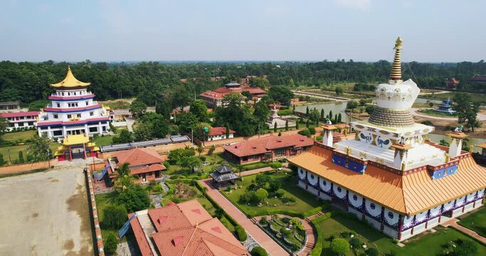 Aerial drone view of a monastic zone featuring a golden-domed temple, a Bhutanese-style stupa and manicured gardens surrounded by trees in Lumbini, Nepal.