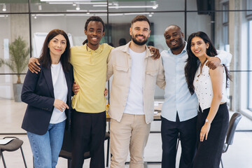 Fototapeta premium Diverse business team smiling, standing together in office, embracing teamwork and partnership for success