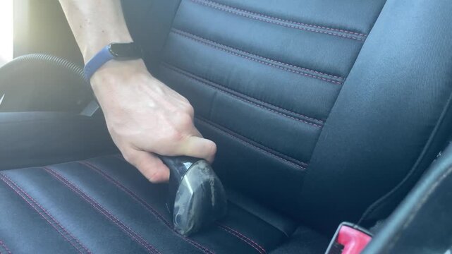 Close up horizontal shot of a person vacuuming a black fabric car seat with red stitching using a wet extraction machine nozzle during a professional detailing process. High quality 4k footage