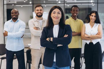 Obraz premium Diverse business team of professionals smiling, a mature female leader standing with arms crossed in front of her colleagues