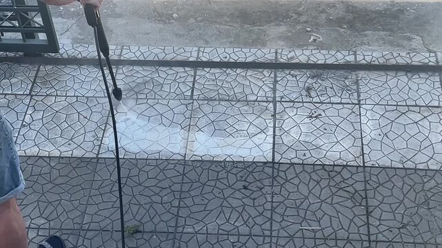 High angle horizontal view of a person cleaning dirty outdoor paving tiles with a high pressure washer nozzle, showing instant removal of dark mud and deep moss. High quality 4k footage