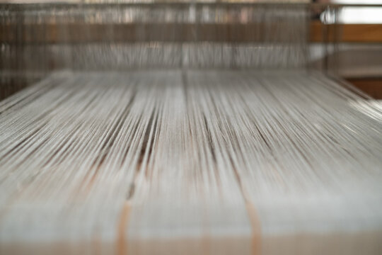 Macro shot of fine warp threads stretched tightly on a traditional wooden loom with shallow depth of field. Authentic Indonesian tenun textile weaving.