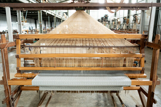 Front wide view of a semi-mechanized traditional loom with punched pattern cards and stretched warp threads. Authentic Indonesian tenun textile manufacturing workshop.