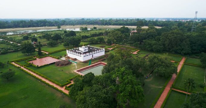 Aerial drone view of the white Maya Devi Temple with its sacred pond and walled gardens surrounded by green trees in Lumbini, Nepal.