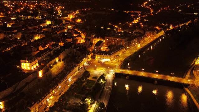 Aerial view of the historic town at night, featuring illuminated streets, buildings, and a bridge over the Oise River in Pontoise, Ile-de-France, France.