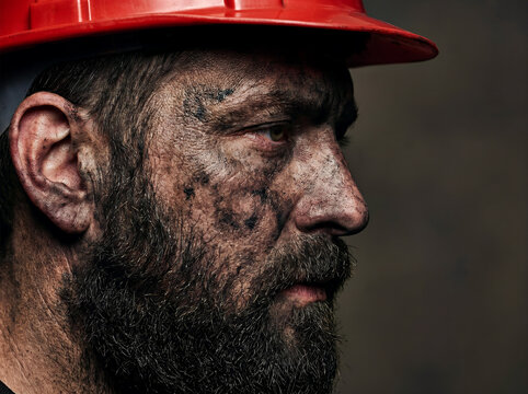 Profile portrait of a male industrial worker with a dirty face wearing a red hard hat