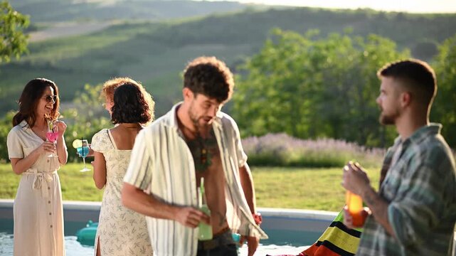 Group of friends talking and drinking at an outdoor summer poolside party during sunset golden hour