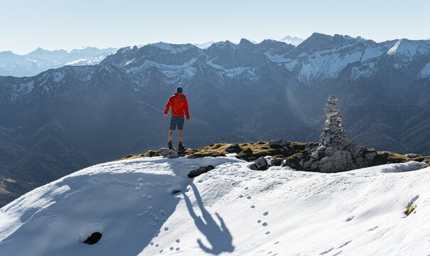 Mountaineer next to a cairn, in front of snowy mountains of the Rofan, hiking trail to the Guffert with first snow, in autumn, Brandenberg Alps, Tyrol, Austria