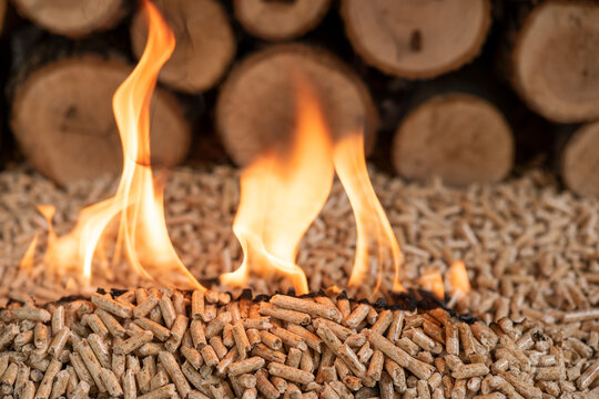 Close Up of Burning Wood Pellets with Flames and Blurred Firewood Background