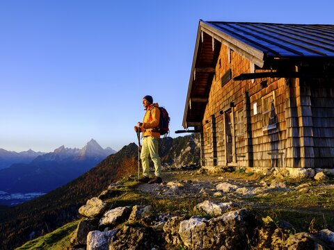 Mountaineer at the Scheibenkaser Almh&uuml;tte in the morning light, behind the Watzmann, Berchtesgaden National Park, Marktschellenberg, Berchtesgadener Land, Upper Bavaria, Bavaria, Germany
