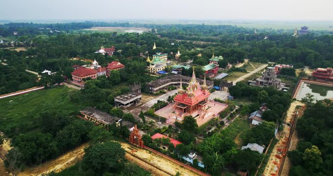 Aerial drone view of an ornate white and gold temple complex surrounded by walls, gardens and green forest in the Lumbini monastic zone, Nepal.