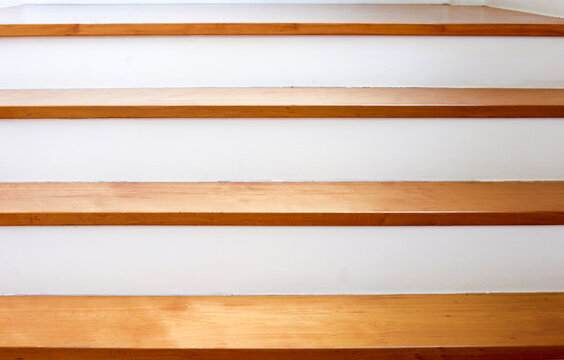 Close-up view of wooden stairs with clean white risers. A minimalist interior design featuring strong horizontal lines, authentic natural wood texture, and soft natural light for background.