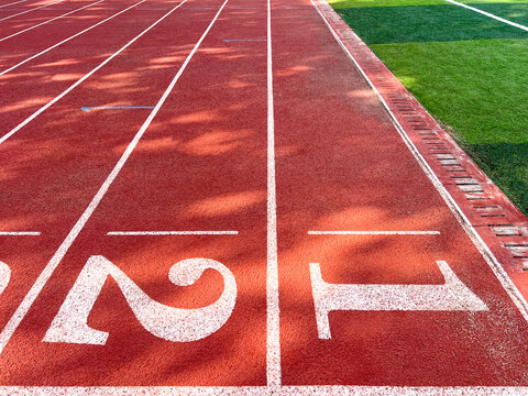Red rubber running track lanes with start numbers 1, 2, 3 and adjacent green artificial grass field. Authentic outdoor stadium surface, ideal for racing, sports training, and competition backgrounds.