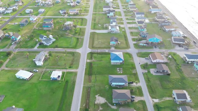 Shoreline residential grid Surfside Beach neighborhood along Seashell Dr presents raised homes arranged beside Gulf facing roadway. Sunlit roofing, bright surf glow river delta, Freeport, Texas
