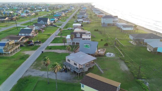 Coastal stilt neighborhood Surfside Beach homes along Seashell Dr align beside Gulf facing corridor with elevated structures near shoreline. Sunlit roofs, bright surf glow frame Freeport, TX