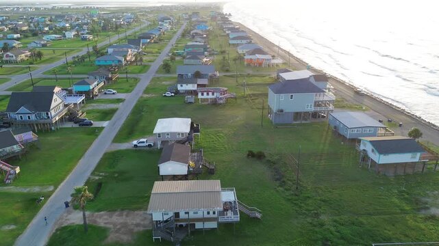 Shoreline parallel streets Surfside Beach blocks near Seashell Dr run beside Gulf edge with raised homes overlooking open water. Warm roofs, vacation rentals, bright surf shimmer in Freeport, TX