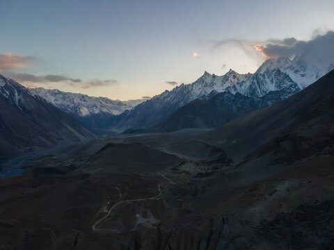 Aerial view of the Karakoram mountain range with snow-capped peaks, rugged valleys, and winding mountain paths at twilight in Hunza Nagar, Gilgit, Pakistan.