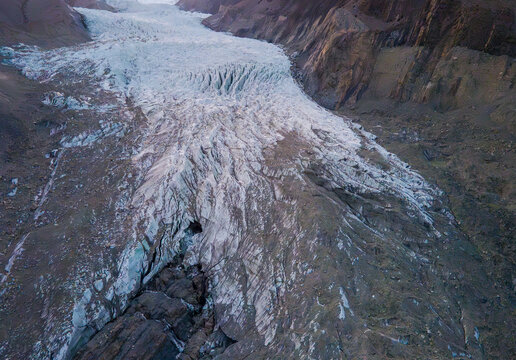 Aerial view of Pasu Glacier showing the rugged ice formations, deep crevasses, and surrounding rocky mountain slopes in Hunza Nagar, Gilgit, Pakistan.