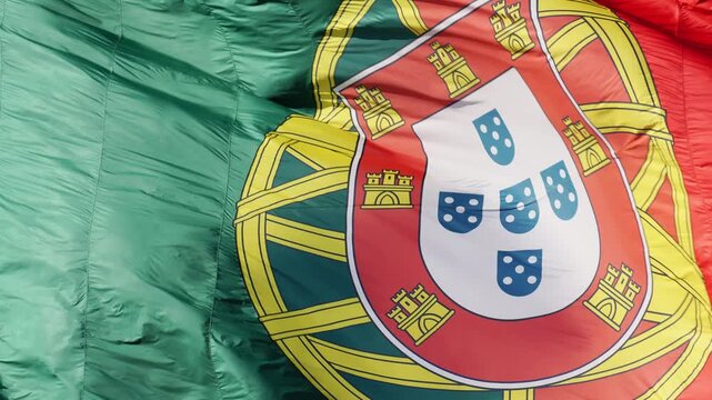 The detailed armillary sphere and official coat of arms filling the frame on a big fluttering flag of Portugal near Edward VII Park in Lisbon. Macro shot
