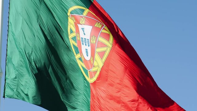 The large flag of Portugal blowing actively in the wind, showcasing its vibrant fabric folds and national emblem near Edward VII Park in Lisbon. Medium close up shot