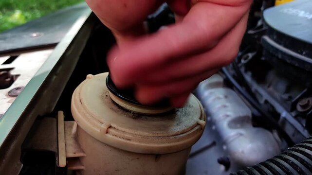 Unscrewing fluid reservoir cap in engine compartment, automotive maintenance activity, vehicle inspection, mechanical service.