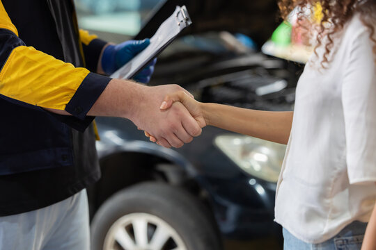 Mechanic and customer shake hands in auto repair shop during daytime in a busy garage