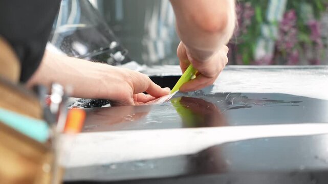 Car wrapping, detailing, tuning and styling. Selective focus. PPF protective film against chips and scratches. A car wrapping specialist applies a polyurethane film to the car. Detailer smoothes PPF. 