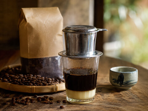 Vietnamese coffee drip beside roasted beans, kraft bags, and a small ceramic cup .generative AI
