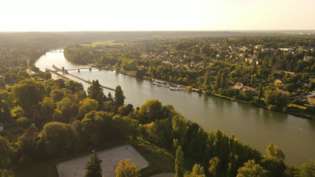 Aerial view of the Seine river winding through the green landscape of Chartrettes, featuring a lock system, small boats, and dense forests. Chartrettes, Ile-de-France, France.
