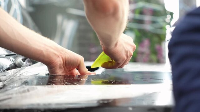 Car wrapping, detailing, tuning and styling. Selective focus. PPF protective film against chips and scratches. A car wrapping specialist applies a polyurethane film to the car. Detailer smoothes PPF. 