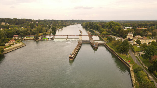 Aerial view of the river lock and dam on the Seine River surrounded by lush trees and residential houses in Chartrettes, Ile-de-France, France.