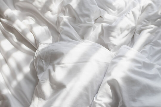 Crumpled white bed sheet pillow sunlight pattern soft bedding texture cozy morning light