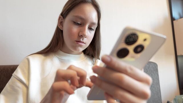 The girl sitting in the room and scrolling with her finger on the screen of her smartphone