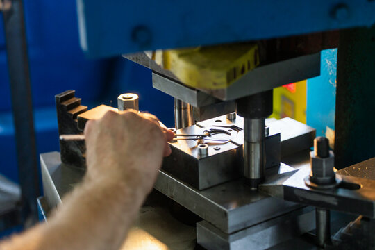 Industrial press stamping metal components in factory workshop. Close-up of manufacturing detail and production process