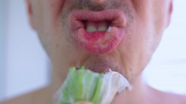 Close up view of an adult man's mouth eating a traditional vietnamese spring roll, also known as gi cun. The healthy, fresh food is being chewed, showcasing the concept of enjoying cuisine
