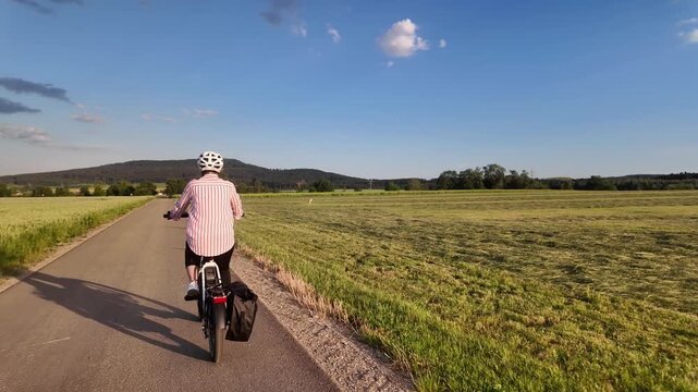 Middle aged woman riding electric bicycle on paved path through green fields