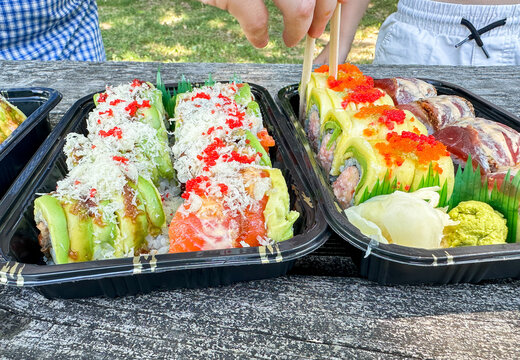 People enjoying fresh sushi rolls outdoors using chopsticks