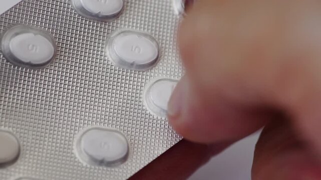 A macro close up of hands popping open and taking a medicine tablet from a blister pack.