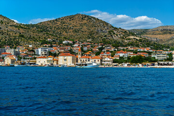 Fototapeta premium Scenic view of the coastal town of Seget Donji near Trogir, Croatia, with traditional stone houses, boats in the harbor, and hills in the background under a blue sky