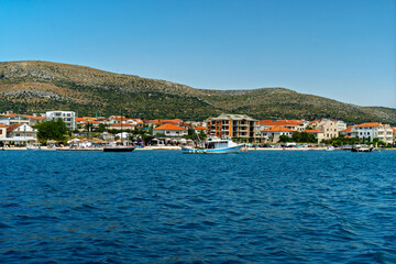 Fototapeta premium Scenic view of a coastal town in Croatia with red-roofed houses, boats in the harbor, and a mountain backdrop under a clear blue sky