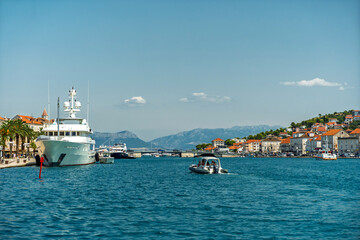 Fototapeta premium Luxury yacht moored at the waterfront of Trogir, Croatia, with historic buildings and mountains in the background under a clear blue sky