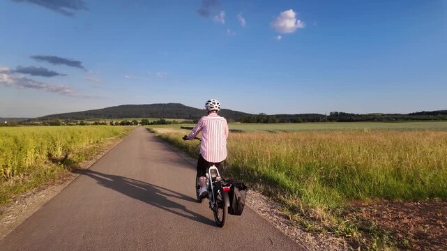 Middle aged woman riding electric bicycle on paved path through green fields