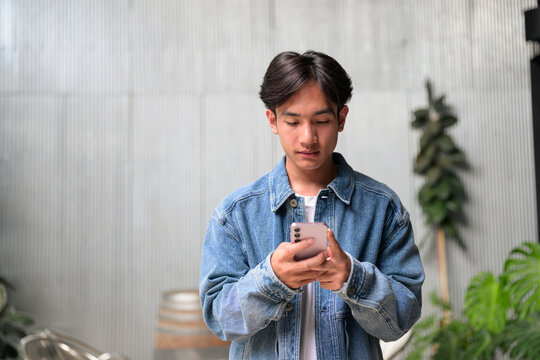 Young Asian non-binary man using phone by corrugated wall wide